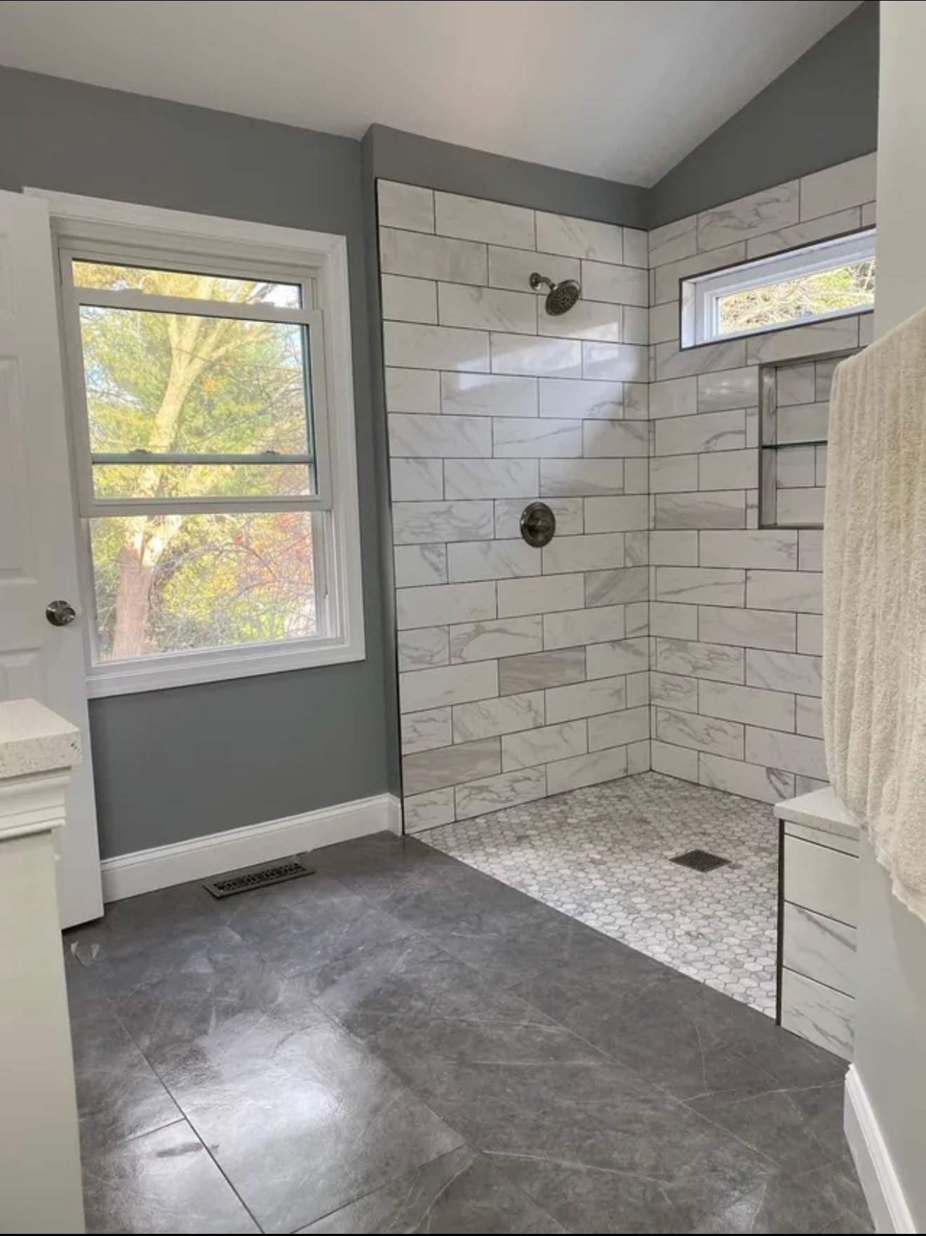 Modern marble-tiled shower with black rainfall showerhead and built-in shelf above a mosaic floor drain