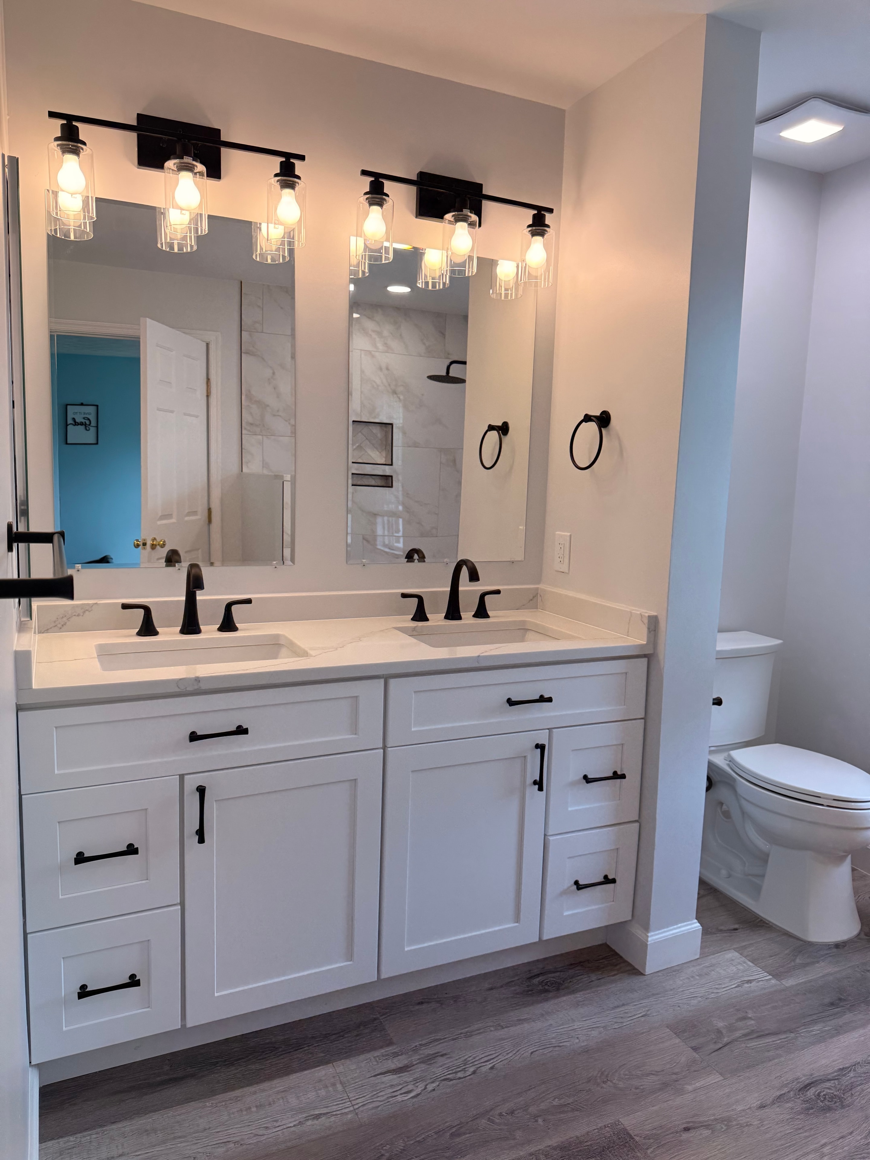 Bathroom vanity with triple mirrors and lights beside a white toilet on wood-look flooring