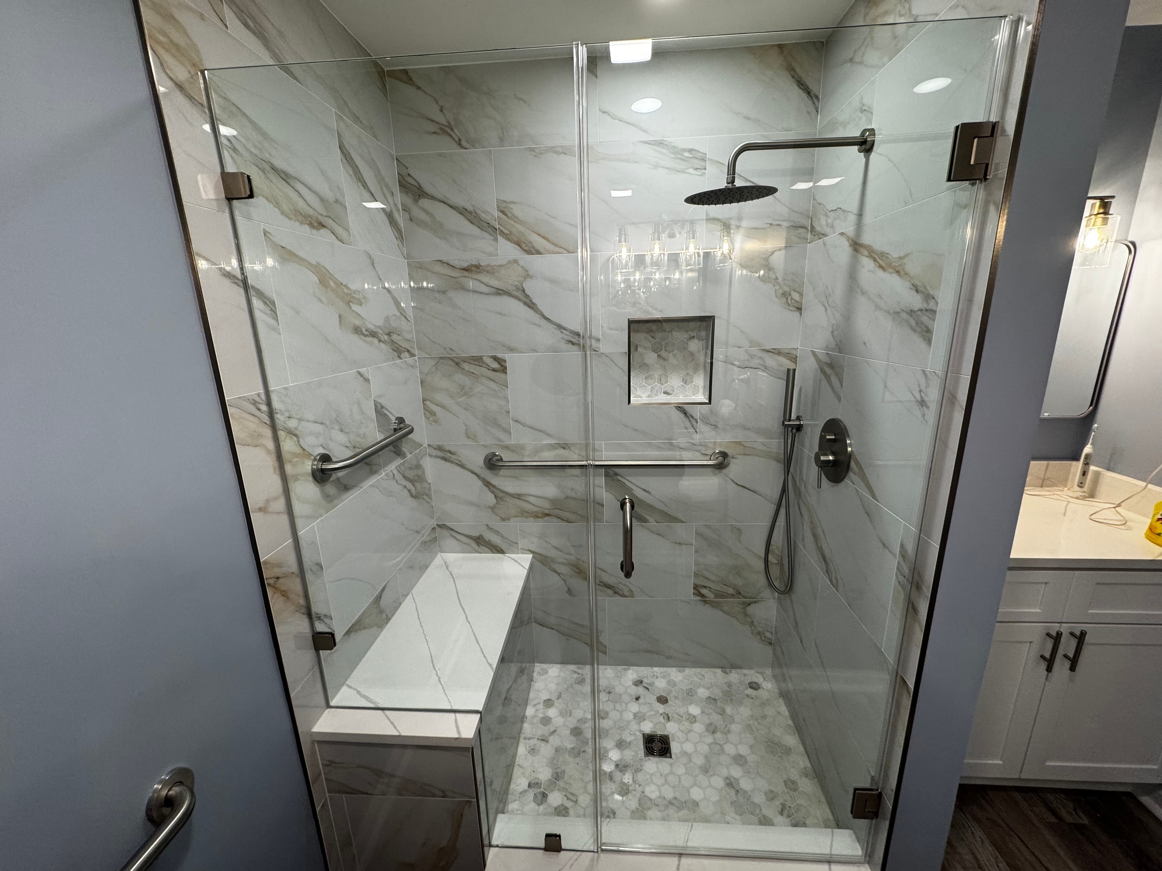 Modern bathroom with freestanding oval tub, large window, dark floor, and glass shower on the left